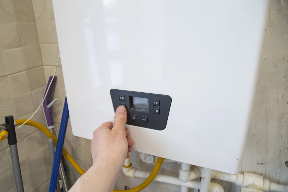 Artisan en vêtement de travail professionnel équipé d'outils, positionné entre deux éléments : d'un côté une armoire électrique murale ouverte montrant des installations électriques résidentielles, de l'autre côté une pompe à chaleur ou un système de chauffage domestique. L'artisan regarde l'appareil photo avec une expression professionnelle confiante. La scène se déroule dans un environnement intérieur résidentiel clair et moderne. Cette composition doit clairement évoquer les deux compétences complémentaires sans texte ni logo visible.